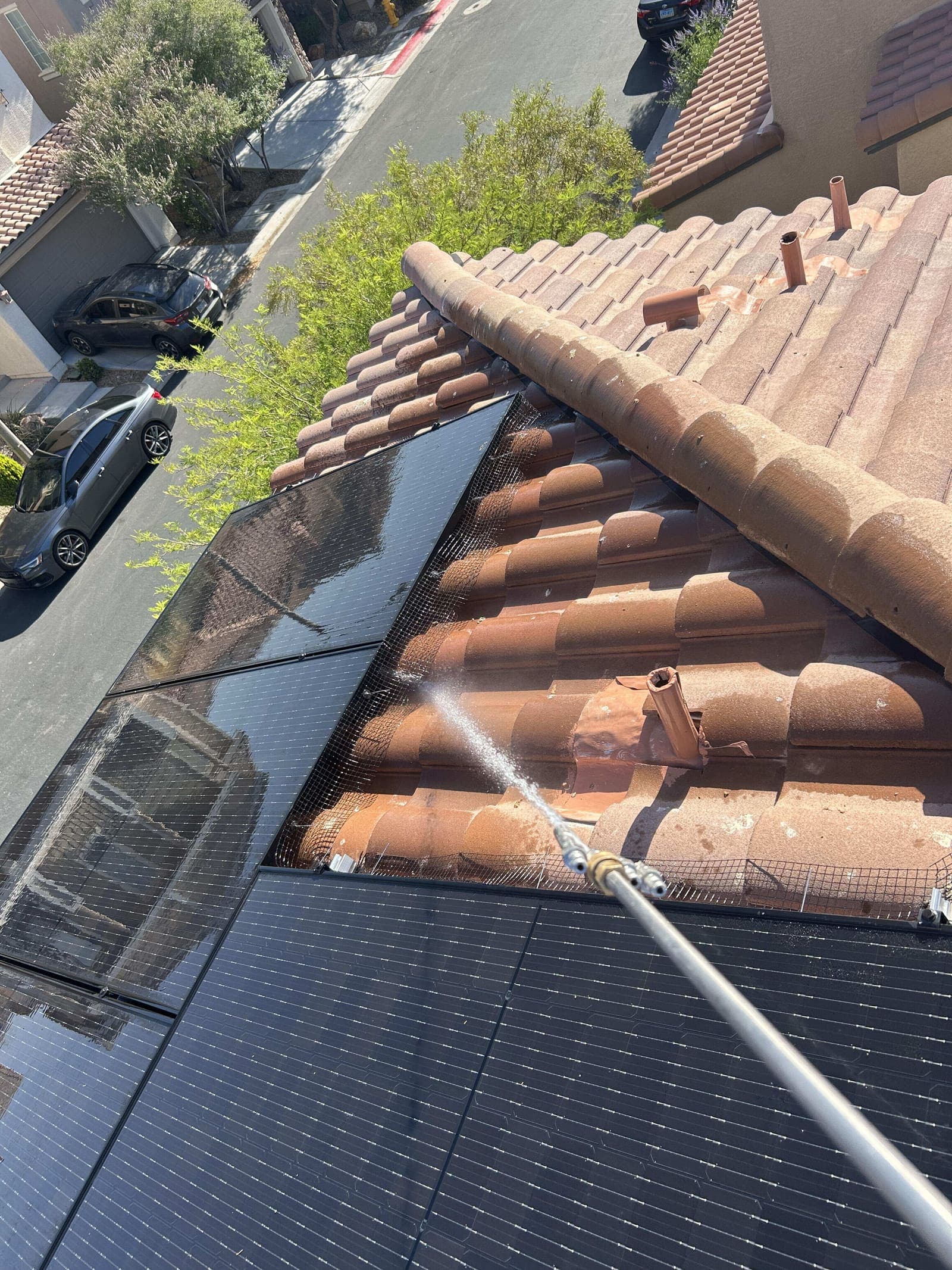 Wide street view of a technician pressure washing a tile roof